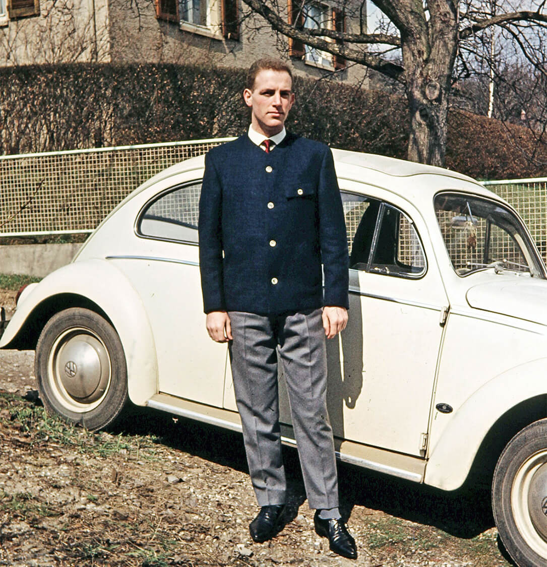 Siegmar Regelmann steht in eleganter Kleidung vor seinem VW Käfer