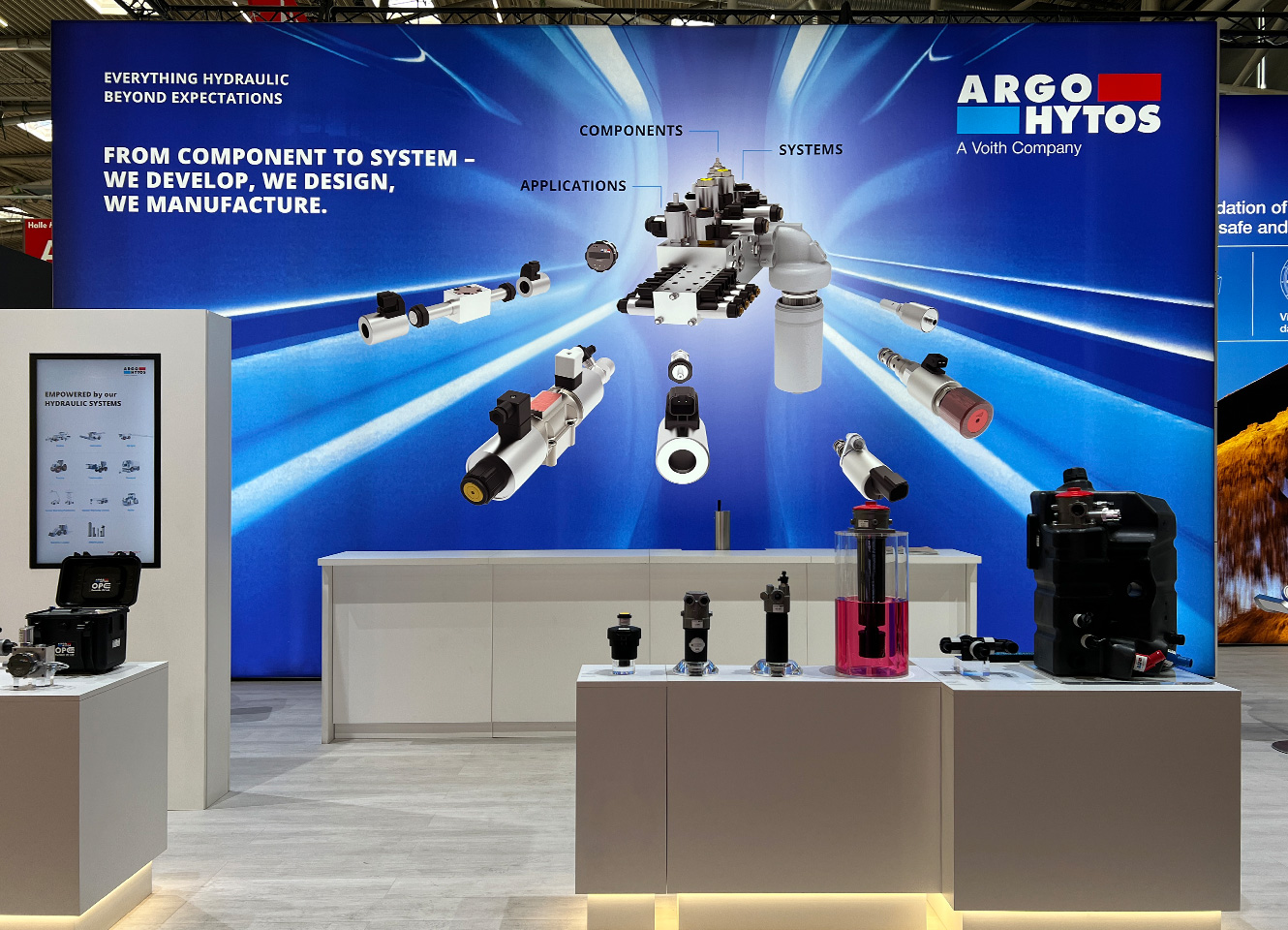 ARGO-HYTOS Messestand mit CI-konformer Rückwand in Blau, Exponaten auf weißen Podesten und prominentem 3D-Komponentenlayout.