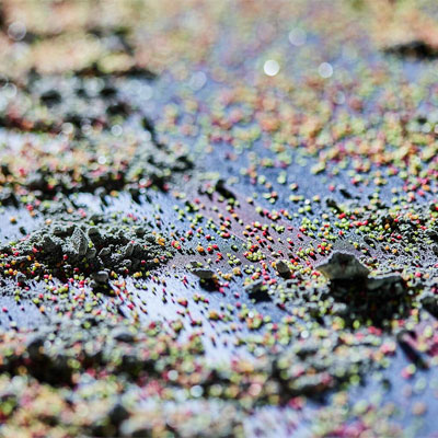 Nahaufnahme bunter Kunststoffgranulate auf reflektierender Oberfläche, Fokus auf Textur und Farbenvielfalt.