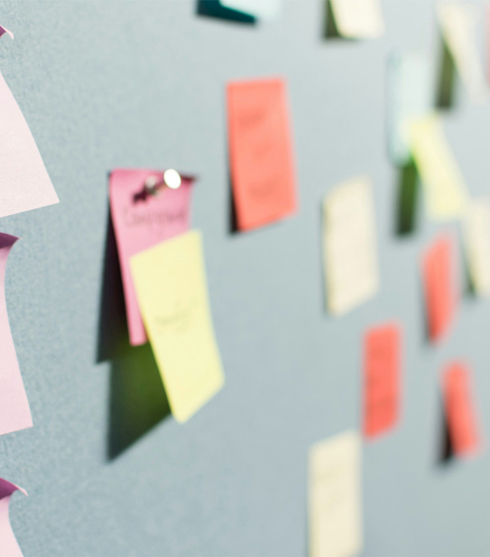 Unscharfer Blick auf eine blaue Wand mit vielen bunten Post-its. Symbolisiert Brainstorming- oder Strategieprozesse.