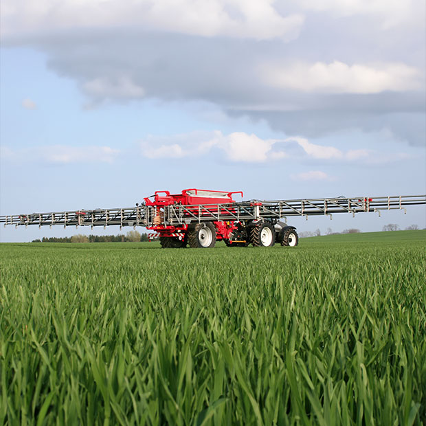 Eine landwirtschaftliche Streumaschine fährt bei gutem Wetter über ein grünes Feld