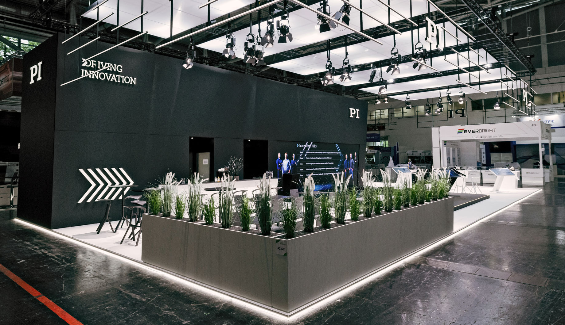 Großer, modern gestalteter Messestand mit Lounge-Bereich, LED-Wand und „Driving Innovation“-Slogan.