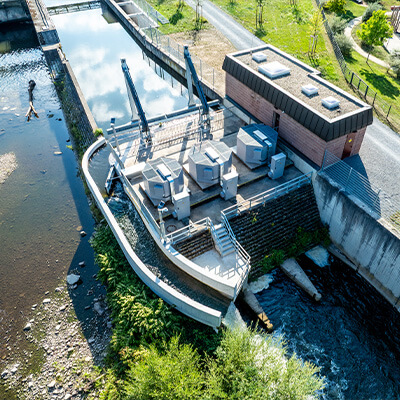 Wasserkraftwerk an einem Fluss mit Wehr, Gebäuden und Grünflächen.