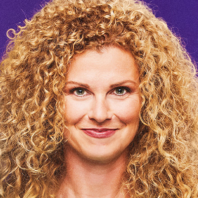 Porträt einer lächelnden Frau mit blonden Locken vor violettem Hintergrund.“