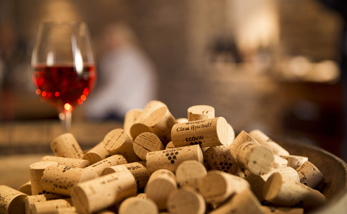 Weinkorken liegen auf Holzfass. Im Hintergrund steht ein Glas mit Roséwein.